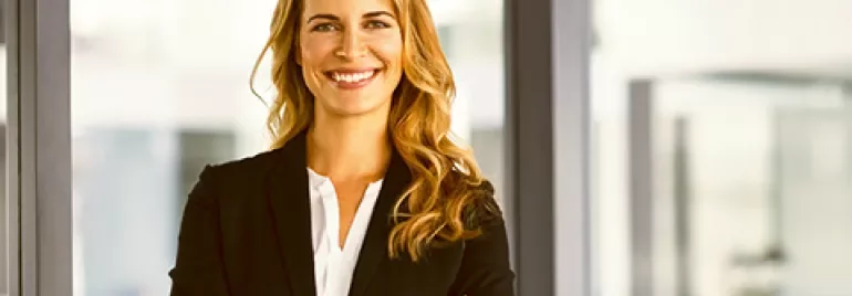 Person in a business suit smiling with arms crossed indoors.
