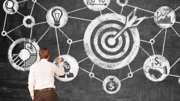 Person drawing a flowchart on a blackboard with target symbols and graphs.