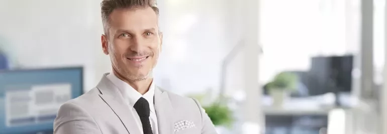 Smiling person in a light gray suit standing in a modern office.