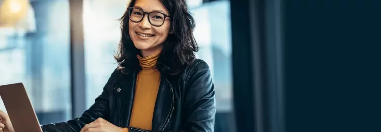 Person with glasses smiling and using a laptop indoors.