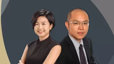 Two professionals smiling in formal attire against a geometric background.